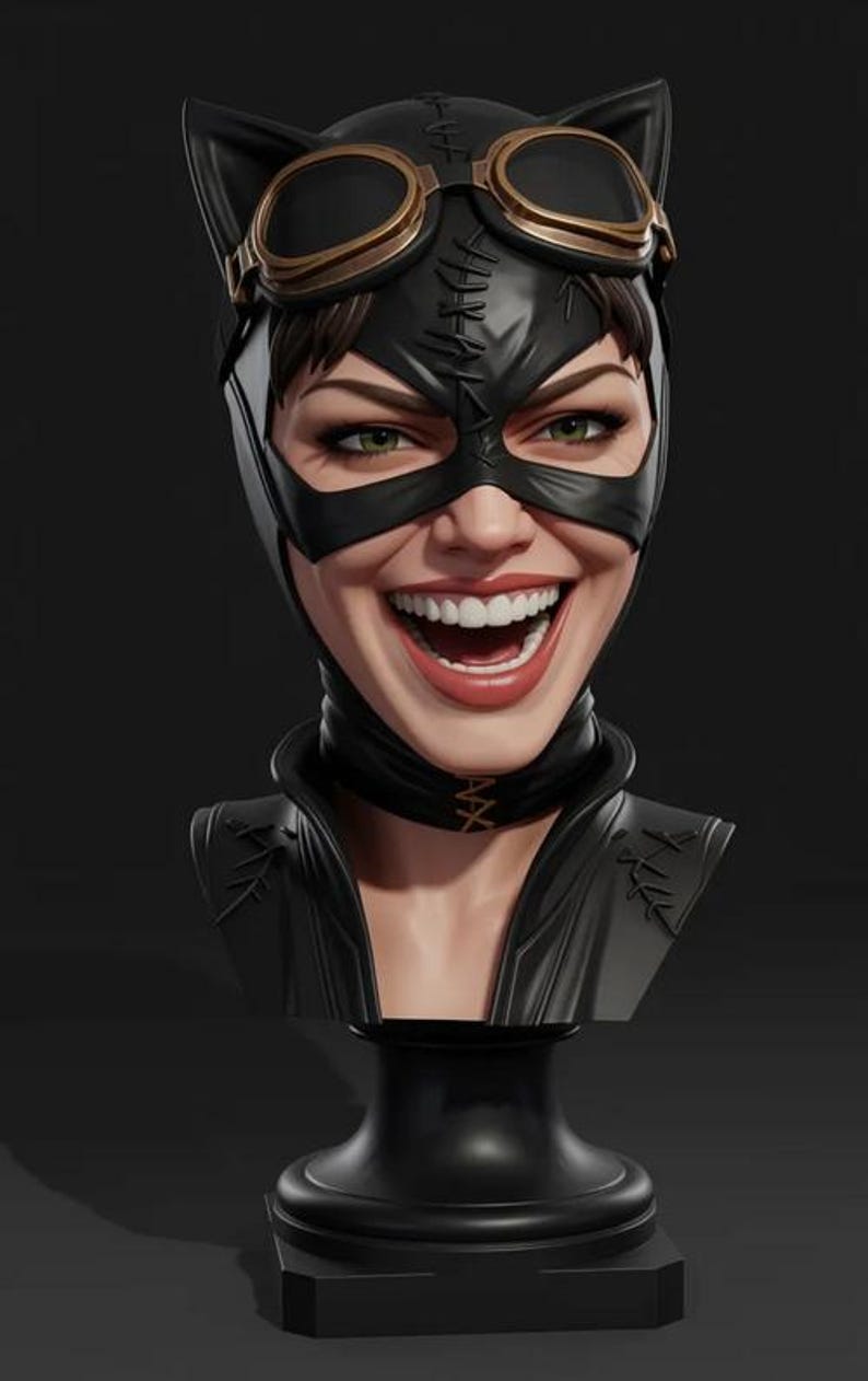 May include: A bust of Catwoman, with a black mask, goggles, and cat ears. The figure has green eyes and a wide smile. The bust is on a black pedestal. The mask has a stitched design.