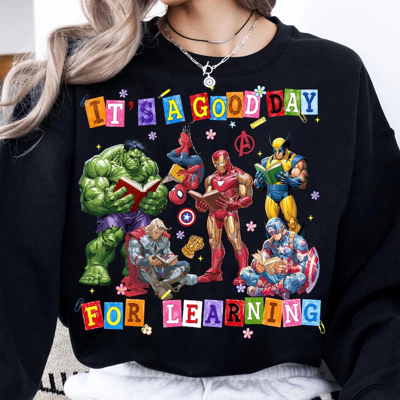 May include: A black crewneck sweatshirt featuring a graphic of Marvel superheroes including Hulk, Spider-Man, Iron Man, Wolverine, Thor, and Captain America reading books. The text reads IT'S A GOOD DAY FOR LEARNING in colorful block letters.