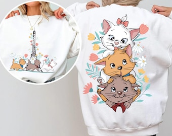 Puede incluir: Una sudadera blanca con un gráfico de tres gatitos apilados verticalmente, rodeados de flores coloridas. La parte delantera muestra a los mismos gatitos caminando hacia la Torre Eiffel. Los gatitos son blancos, naranjas y grises con lazos.