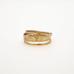 Puede incluir: Un anillo de oro hecho de cinco bandas delgadas apiladas una encima de la otra. Las bandas están martilladas y tienen una superficie texturizada.