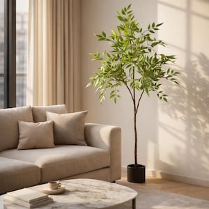 May include: A living room scene featuring a beige sectional sofa with throw pillows, a round marble coffee table, and a tall artificial tree in a black pot. The tree has green leaves and a brown trunk. Soft sunlight streams through the window.