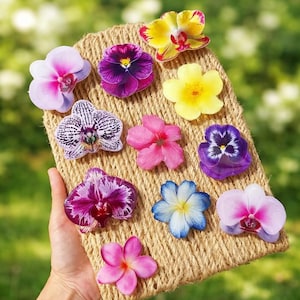 May include: A collection of colorful flower cutouts, including orchids and pansies, are arranged on a woven, rectangular surface. The flowers display a variety of colors, such as pink, purple, yellow, and blue. The arrangement is held by a hand.