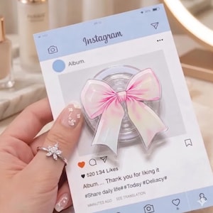 May include: A light blue Instagram-themed card with a pink and white bow-shaped phone grip. The card displays the Instagram interface, including the word "Instagram", a heart icon, and the text "520 134 Likes".