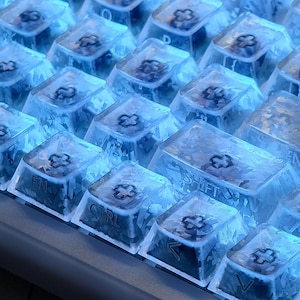 May include: Close-up of a backlit mechanical keyboard with transparent keycaps. The keycaps have a frosted appearance and are illuminated with a cool blue light. The keys include "CTRL", "SHIFT", and "FN".