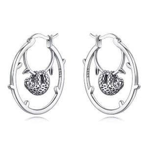 May include: A pair of silver hoop earrings featuring a small, detailed sloth hanging from a branch-like design within the hoop. The metal is stamped with S925, indicating sterling silver composition. The earrings have a polished finish and secure clasps.