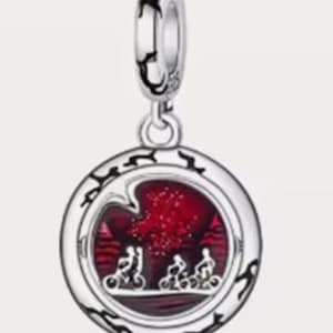 May include: Silver-toned charm with a round pendant featuring a red background with a silhouette of three figures on bicycles. The charm has a decorative border and a loop for attachment.