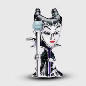 May include: A silver-toned metal charm featuring a stylized character with two prominent horns, a pale face, and bright red lips. The figure wears a dark, glittery robe and holds a long staff topped with a light blue sphere in one hand.