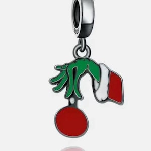 May include: Silver charm with a green hand holding a red ornament. The charm has a white and red cuff. The charm is a Christmas-themed accessory.