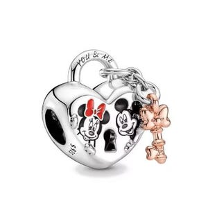 May include: A silver heart-shaped padlock charm featuring the engraved text YOU & ME on the shackle and S925 on the side. The front displays black and white illustrations of Minnie and Mickey Mouse with a red bow. A rose gold-toned key charm is attached.