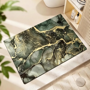 May include: Rectangular bath mat with a marble design. The mat features a blend of dark green, black, and gold colors, creating a luxurious aesthetic. The design resembles flowing ink or paint, adding a touch of elegance to any bathroom.