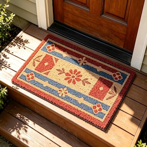 May include: Rectangular doormat with a floral and geometric design. The mat features a red border, blue stripes, and tan center with red floral and geometric patterns. Placed on wooden steps near a brown door.