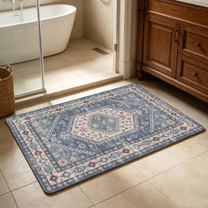 May include: A rectangular blue bathroom rug with an intricate geometric pattern. The rug features a central medallion design in shades of cream, pink, and blue, surrounded by a border of repeating floral and geometric motifs. The rug is placed on a tiled floor.