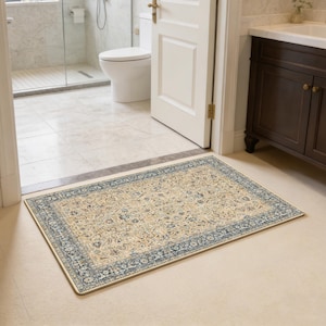 May include: Rectangular beige rug with a detailed floral pattern and a dark blue border. The rug is placed in a bathroom doorway, adding a touch of elegance to the space. The rug's design features intricate floral motifs.
