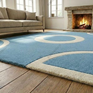 May include: A light blue area rug with a circular design in off-white. The rug is placed on a hardwood floor, with a sofa and fireplace in the background. The rug's design adds a modern touch to the room.