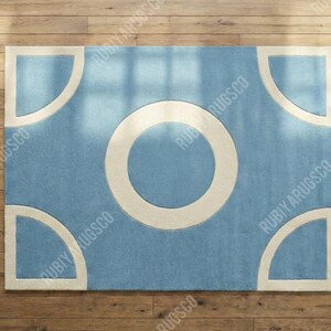 May include: A rectangular rug with a light blue field and a large white circle in the center. Four white quarter-circle shapes are in each corner. The rug is on a wooden floor.
