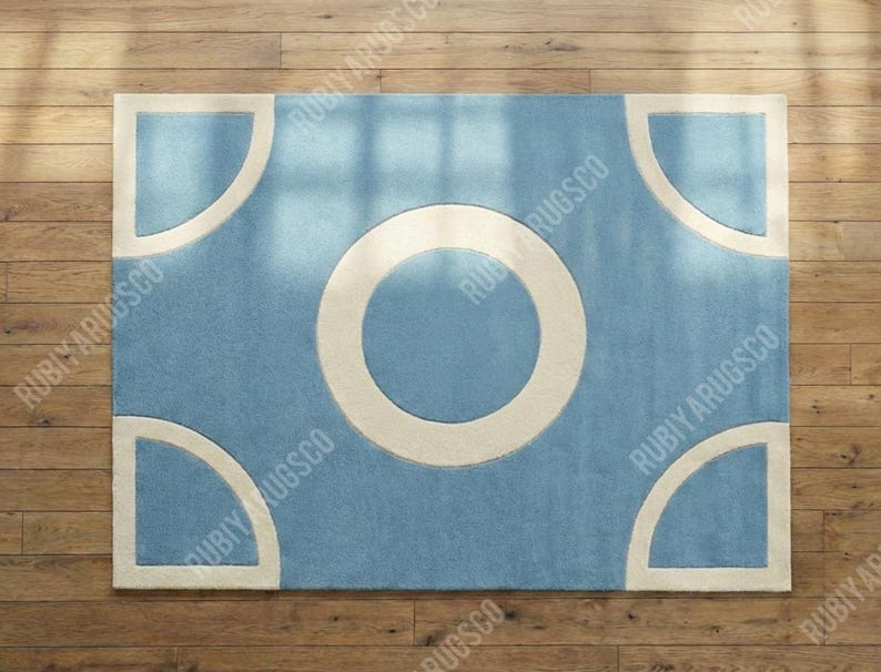 May include: A rectangular rug with a light blue field and a large white circle in the center. Four white quarter-circle shapes are in each corner. The rug is on a wooden floor.
