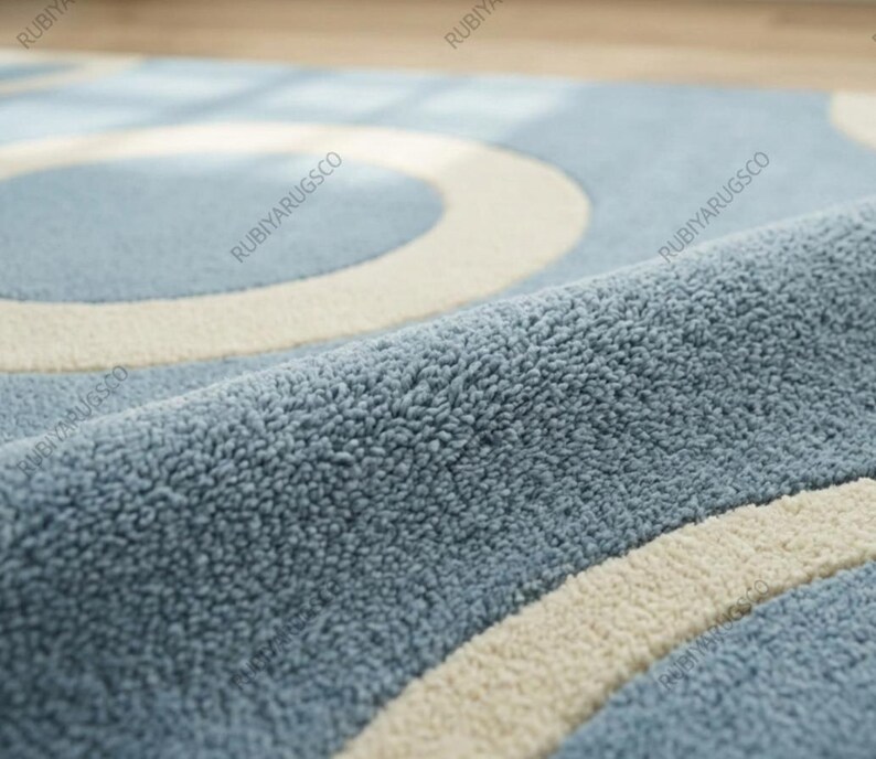 May include: Close-up of a blue rug with a cream-colored circular pattern. The rug has a soft, textured surface. The design features overlapping circles, creating a modern aesthetic. The rug's color palette is a mix of light blue and cream.
