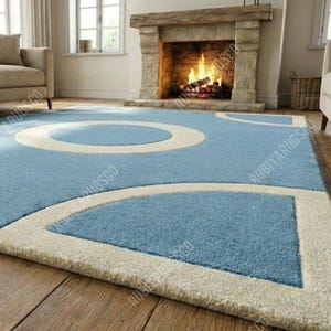 May include: A light blue area rug with a geometric design featuring large white circles and curved shapes. The rug is placed on a hardwood floor in front of a fireplace. The rug's design adds a modern touch to the room.
