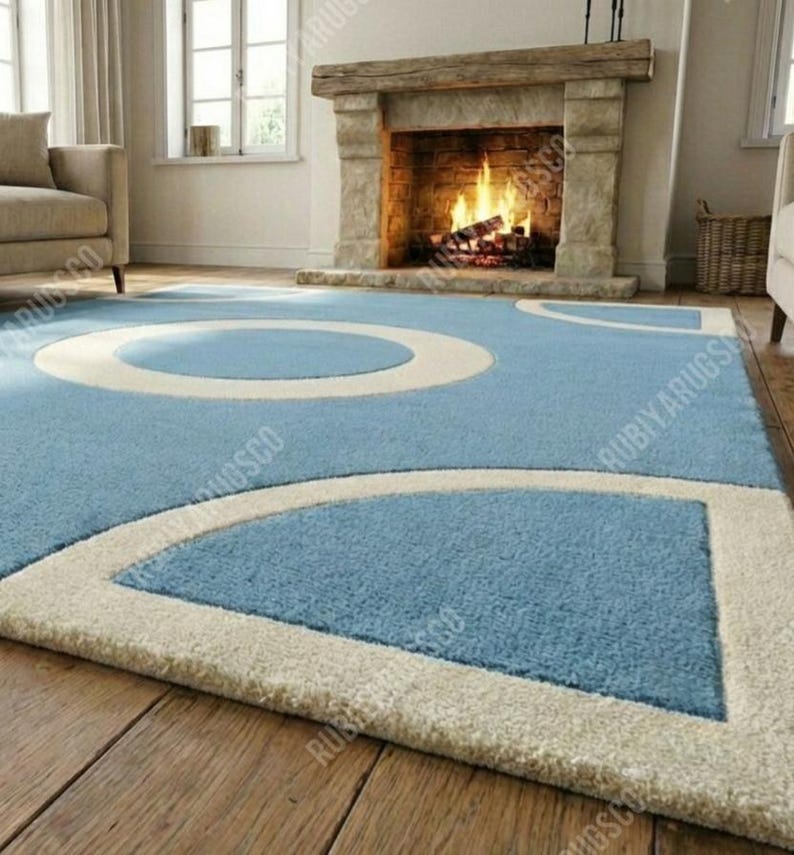 May include: A light blue area rug with a geometric design featuring large white circles and curved shapes. The rug is placed on a hardwood floor in front of a fireplace. The rug's design adds a modern touch to the room.