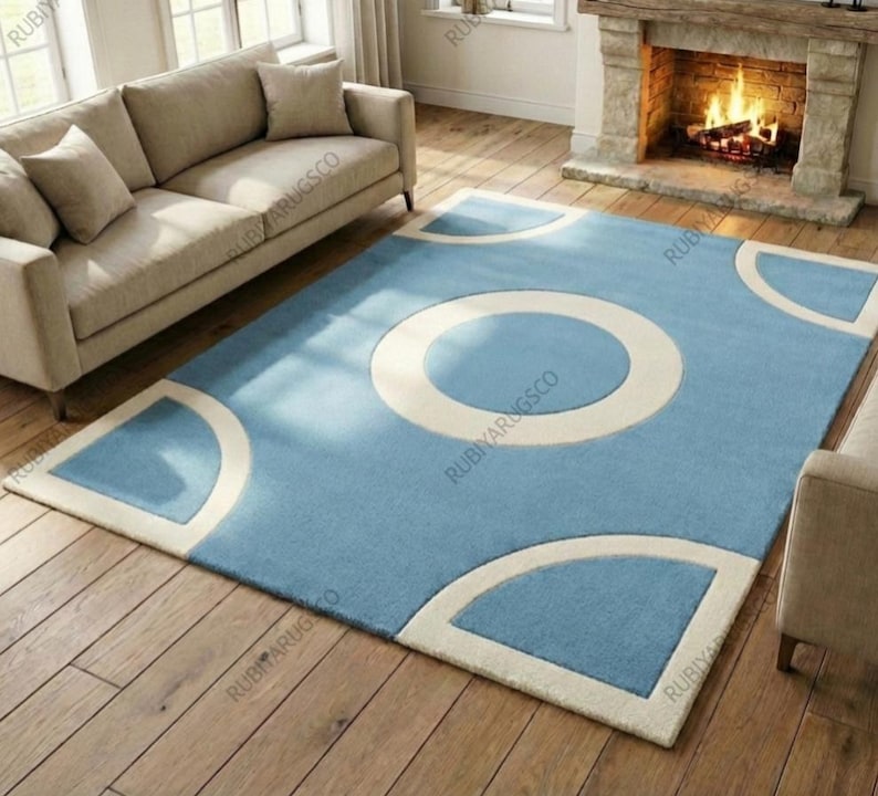 May include: A rectangular blue area rug with a large white circle in the center and white geometric shapes at the corners. The rug is placed on a hardwood floor in a living room setting.