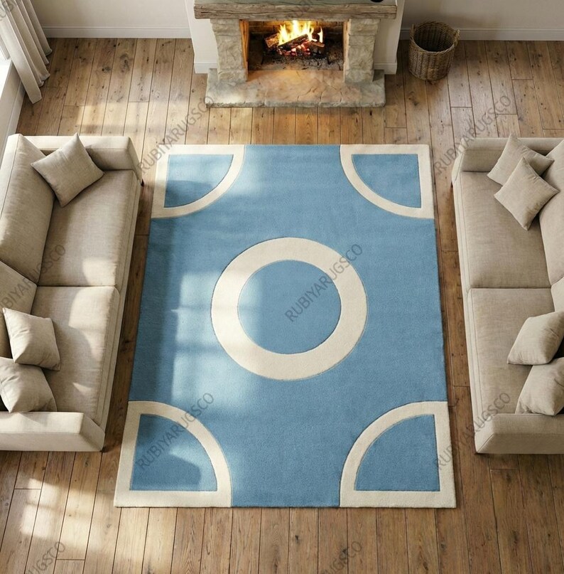 May include: A rectangular blue rug with a large off-white circle in the center and four quarter-circle shapes in the corners. The rug is placed on a wooden floor, with two beige sofas on either side. A fireplace is visible in the background.