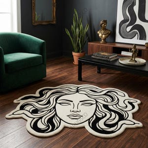 May include: A circular area rug featuring a black and white line art illustration of a face with flowing, snake-like hair. The rug has an irregular, organic shape that follows the contours of the hair and face design, creating a bold graphic contrast.
