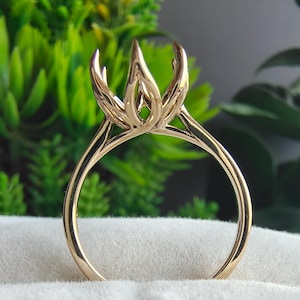 May include: A gold ring setting featuring a high, multi-prong head designed to hold a center stone. The band is smooth and polished, with a slender profile that tapers upward toward the intricate, petal-like prongs that extend from the base.