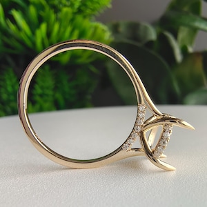 May include: A gold ring featuring a thin band with a series of small, clear pavé-set stones along the side and a prominent, elevated prong setting designed to hold a central gemstone, showcasing a polished metallic finish and intricate detailing.