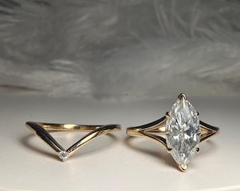 May include: A gold ring set featuring a marquise-cut center stone held by a split shank and a matching V-shaped chevron band with a single small round stone at the point. Both rings are crafted from polished yellow gold with clear stones.