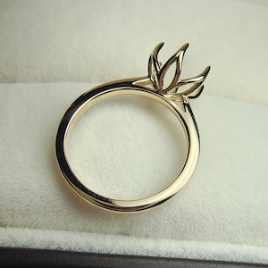 May include: A polished yellow gold ring setting featuring a six-prong head designed to hold a gemstone. The band is smooth and circular, showcasing a high-shine metallic finish. The setting is empty, waiting for a stone to be mounted securely.