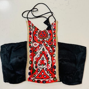 May include: A red, white, and black embroidered bag with a black strap. The bag features intricate patterns and mirrored accents. The edges are trimmed with gold-colored fabric, and the bag is paired with a black velvet pouch.