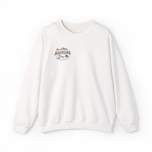 Op de afbeelding: Een witte crewneck sweatshirt met een kleine afbeelding op de borst. De afbeelding toont het woord "Adventure" boven een bergketen, zon, bomen en de tekst "Live Free - Travel Far".