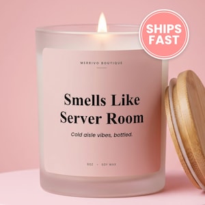 May include: A frosted glass candle with a light pink label featuring the text Merrivo Boutique, Smells Like Server Room, Cold aisle vibes, bottled, and 8oz soy wax. The candle has a lit wick and is accompanied by a separate round bamboo lid.
