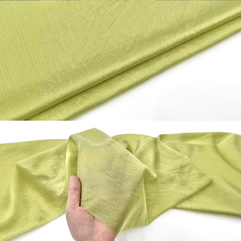 May include: A piece of light green fabric with a subtle, fine-ribbed texture. The material is shown folded and draped, displaying a soft, slightly translucent quality with visible horizontal lines running across the surface of the textile.