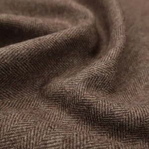 May include: Close-up of brown herringbone fabric with a textured surface. The fabric has a woven pattern with diagonal lines creating a V-shape design. The material appears soft and slightly fuzzy.