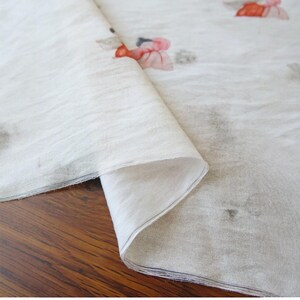 Peut inclure: Tissu blanc cass&eacute; avec un motif floral. Le tissu est pli&eacute;, r&eacute;v&eacute;lant une texture en couches. Le motif floral pr&eacute;sente des fleurs roses et oranges avec des accents gris. Le tissu est probablement du lin ou un mat&eacute;riau l&eacute;ger similaire.