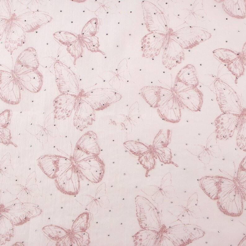 Op de afbeelding: Zachtroze stof met een herhaald patroon van roze vlinders in verschillende maten. De vlinders zijn omlijnd met een donkerder roze en versierd met kleine, verspreide zilveren stippen. De achtergrond is zacht, lichtroze.