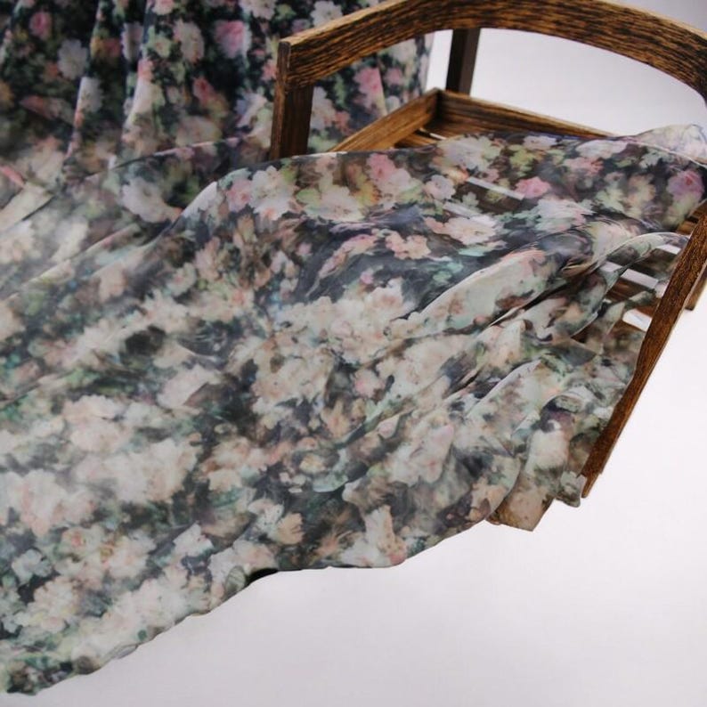 Pu&ograve; includere: Tessuto floreale drappeggiato su una cornice di legno. Il tessuto presenta un motivo di piccoli fiori colorati su sfondo scuro. I fiori sono nelle tonalit&agrave; del rosa, bianco e verde.