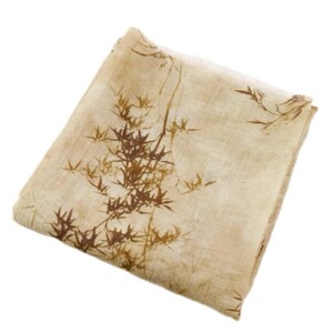 May include: A folded beige scarf with a brown bamboo leaf pattern. The scarf is made of a lightweight fabric and has a natural, organic aesthetic. The bamboo design is detailed and adds a touch of nature-inspired elegance.