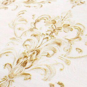 May include: Close-up of a white fabric with a repeating gold damask pattern. The design features ornate, swirling floral and leaf motifs, creating a textured, elegant appearance. The fabric has a subtle sheen, enhancing the gold details.