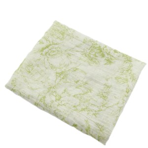 May include: A folded, off-white fabric with a repeating floral pattern in shades of green. The design features stylized roses and other botanical elements, creating a soft, textured appearance. The fabric appears lightweight and suitable for various uses.