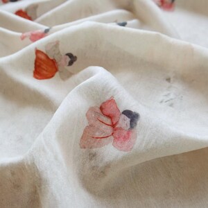 Peut inclure: Gros plan sur un tissu blanc cass&eacute; avec un motif floral &agrave; l'aquarelle. Le motif pr&eacute;sente des motifs de fleurs rouges, roses et grises dispers&eacute;s sur la surface. Le tissu est l&eacute;g&egrave;rement pli&eacute;, montrant sa texture.