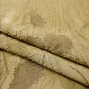 Pode incluir: Um tecido castanho claro com uma textura enrugada e um padr&atilde;o bot&acirc;nico subtil de folhas em castanho escuro. O material apresenta uma apar&ecirc;ncia suave e org&acirc;nica com dobras e vincos vis&iacute;veis em toda a superf&iacute;cie do tecido.