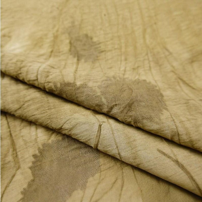 Pode incluir: Um tecido castanho claro com uma textura enrugada e um padr&atilde;o bot&acirc;nico subtil de folhas em castanho escuro. O material apresenta uma apar&ecirc;ncia suave e org&acirc;nica com dobras e vincos vis&iacute;veis em toda a superf&iacute;cie do tecido.