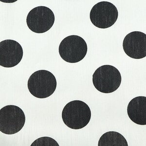 May include: Close-up of a white fabric with a repeating pattern of large, evenly spaced black polka dots. The dots are solid black and circular, creating a high-contrast design. The fabric appears to be lightweight.