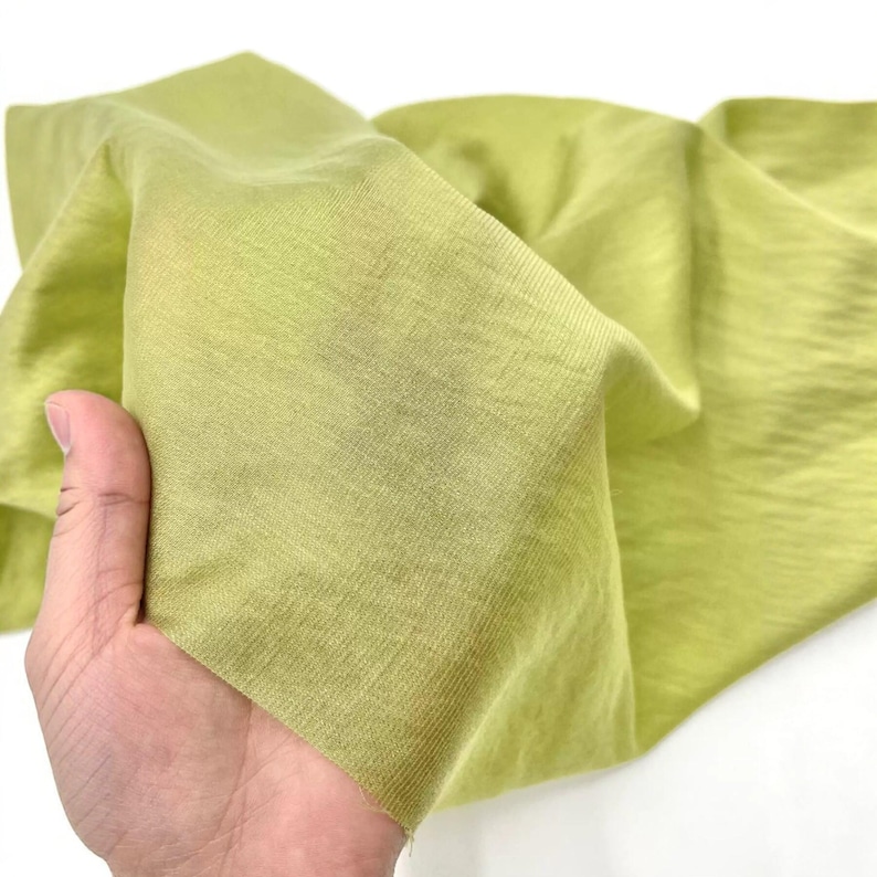 May include: A piece of lightweight, semi-sheer fabric in a vibrant lime green color. The material features a fine, visible knit texture with a soft drape, showing subtle variations in tone where the fabric folds and catches the light.