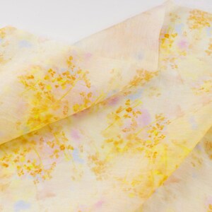 May include: A folded piece of fabric with a floral pattern. The fabric is primarily a pale yellow color, with a delicate pattern of yellow and orange flowers and hints of pink and blue.