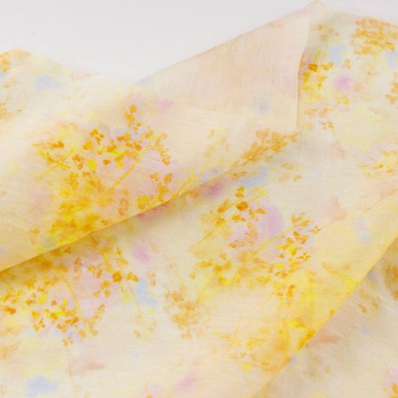 May include: A folded piece of fabric with a floral pattern. The fabric is primarily a pale yellow color, with a delicate pattern of yellow and orange flowers and hints of pink and blue.