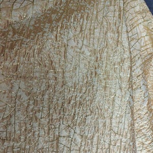 May include: A fabric featuring a textured, crackled pattern in metallic gold and off-white. The surface displays a network of irregular, intersecting lines that create a distressed, weathered appearance across the entire material surface.