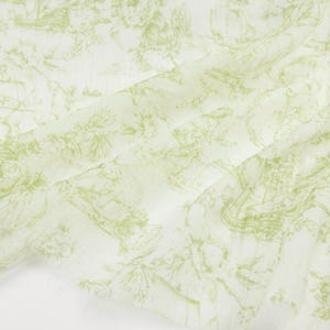 May include: Off-white fabric with a delicate, repeating pattern in light green. The design features a detailed, vintage-style illustration of landscapes, buildings, and floral elements. The fabric has a soft, flowing appearance.